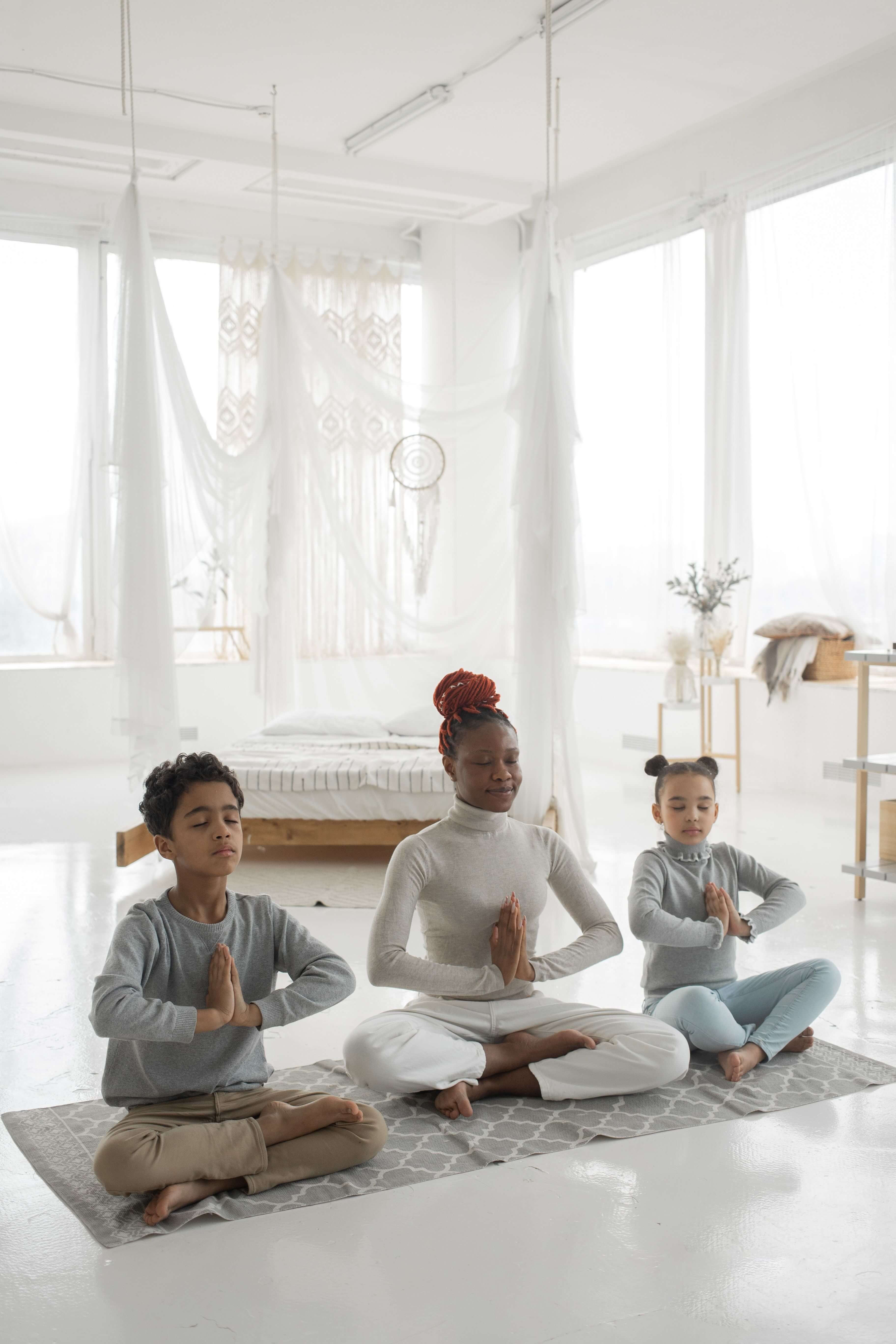 A black mother and two children meditating in a bright, minimalist bedroom for mindfulness practice.